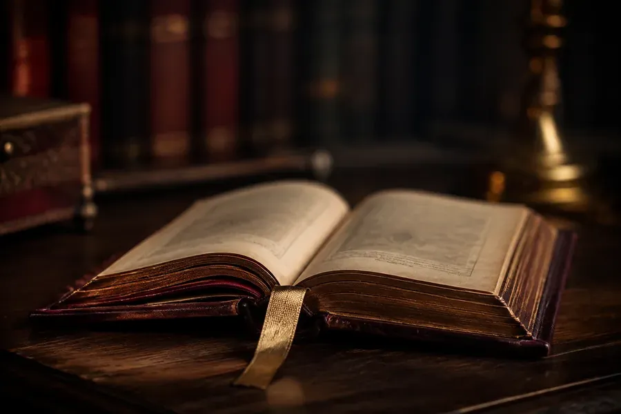 Livre ancien relié de cuir bordeaux, ouvert sur une table de bois sombre